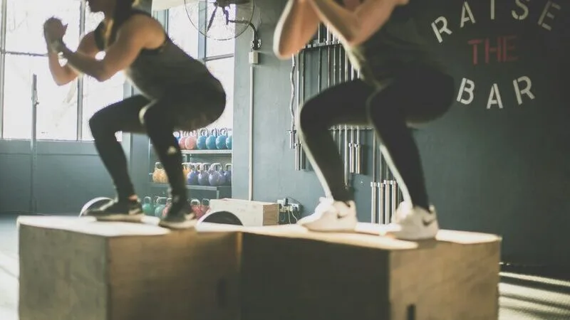 Two members doing box jumps side by side in a CrossFit box