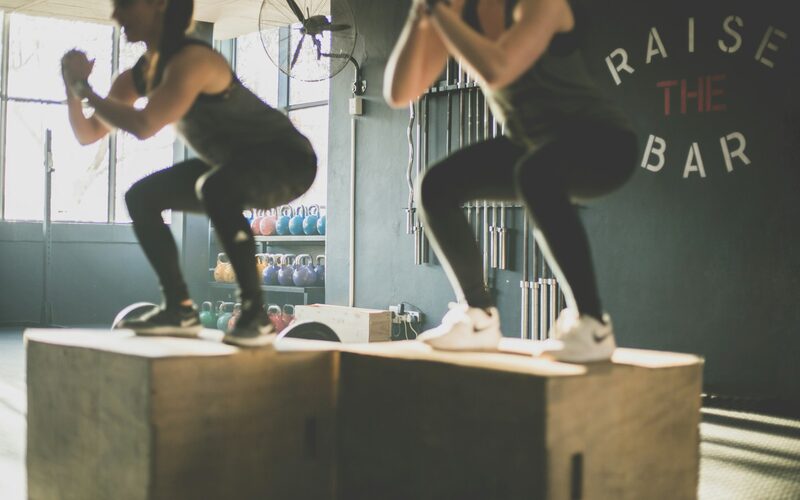 Two members doing box jumps side by side in a CrossFit box